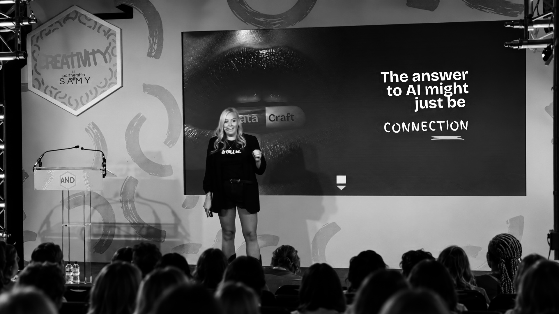 Charlotte Pearce speaking on stage at MADFest, in front of a slide reading: the answer to AI might just be connection